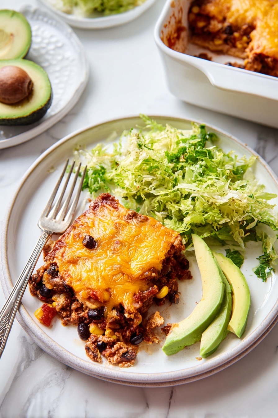 A white round plate shows a square piece of layered casserole with melted orange cheese on top. The casserole has one visible main layer filled with dark beans, corn, and ground meat mixed with tomato sauce. Next to the casserole on the plate is a pile of shredded green lettuce and three slices of avocado with light green flesh. A fork with a piece of the casserole rests on the left side of the plate. The scene is set on a white marbled surface with a halved avocado on a white plate near the top left and a white baking dish with more casserole visible on the top right. photo taken with an iphone --ar 2:3 --v 7