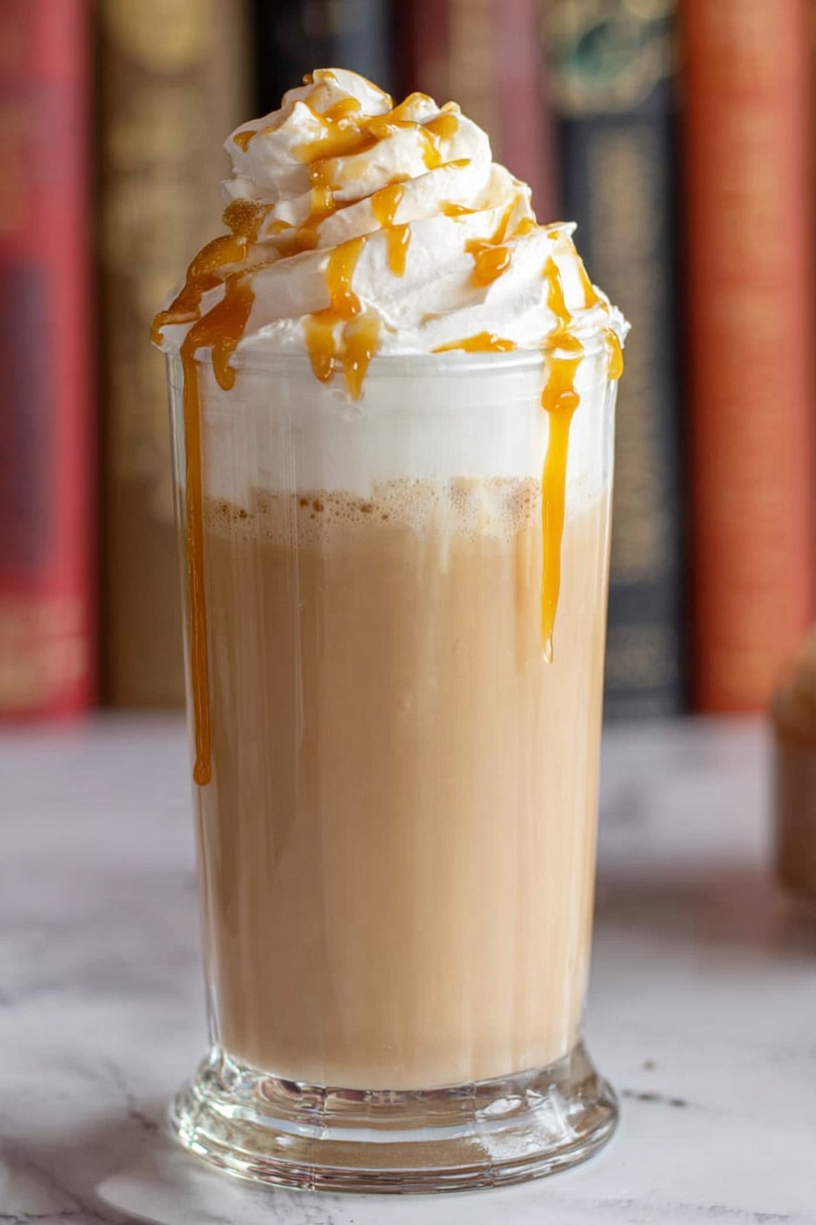 The image shows a tall clear glass filled with a light brown creamy drink as the bottom layer. Above this is a thick layer of white whipped cream piled high, with golden caramel sauce drizzled over it, some of the caramel dripping down the side of the glass. The glass is placed on a white marbled surface with blurry colorful books in the background. photo taken with an iphone --ar 2:3 --v 7