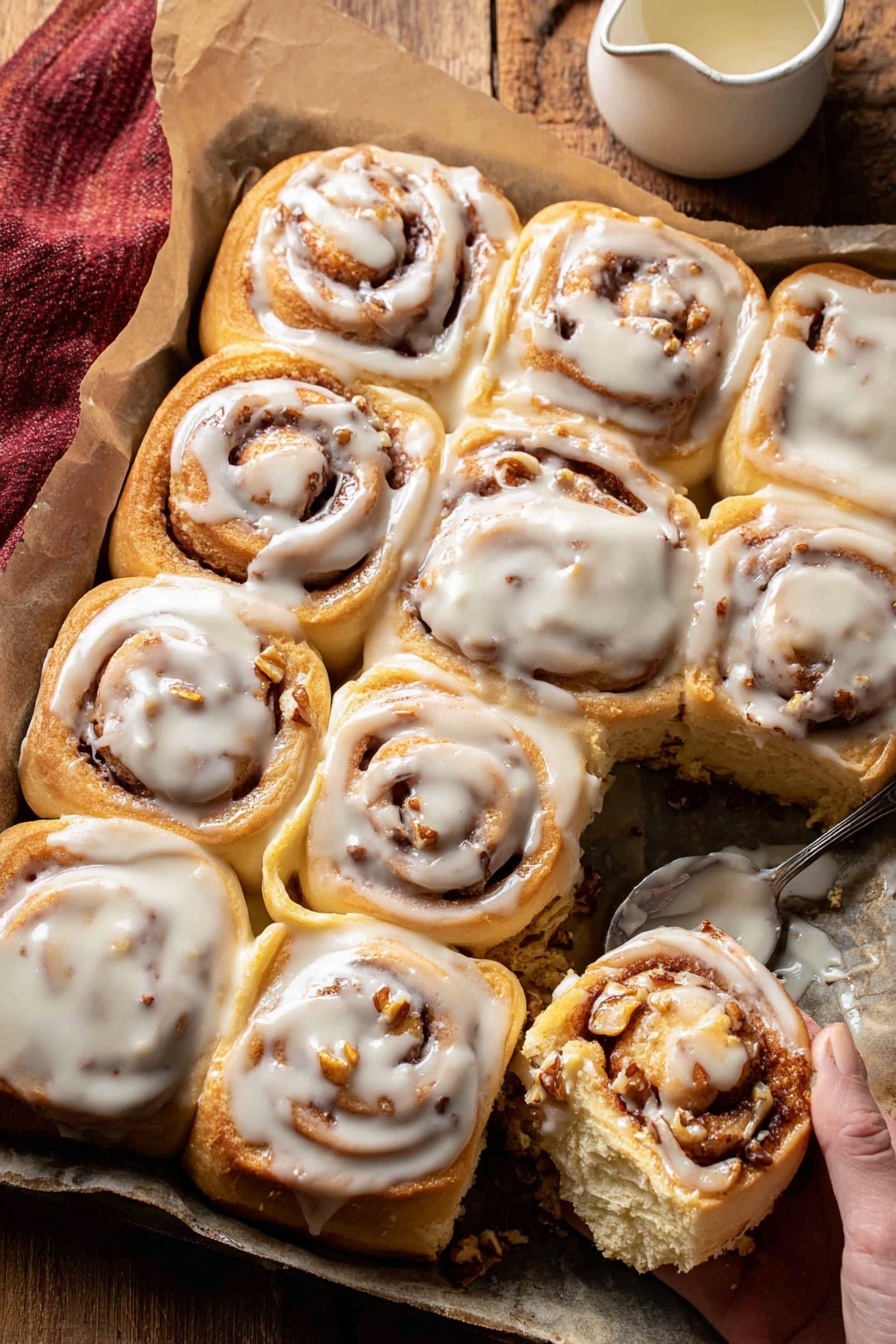 The image shows a tray of twelve warm cinnamon rolls covered in thick white icing. Each roll has a soft, golden-brown dough with visible swirls of cinnamon and small bits of chopped nuts inside. The rolls are closely placed together on a piece of parchment paper, with some of the icing slightly melting over the edges. A woman's hand is holding one cinnamon roll that has been taken away from the group, showing the soft and fluffy texture inside. Nearby, there is a small jug of extra white icing and a spoon with some icing on it, placed on a wooden surface. Photo taken with an iphone --ar 2:3 --v 7