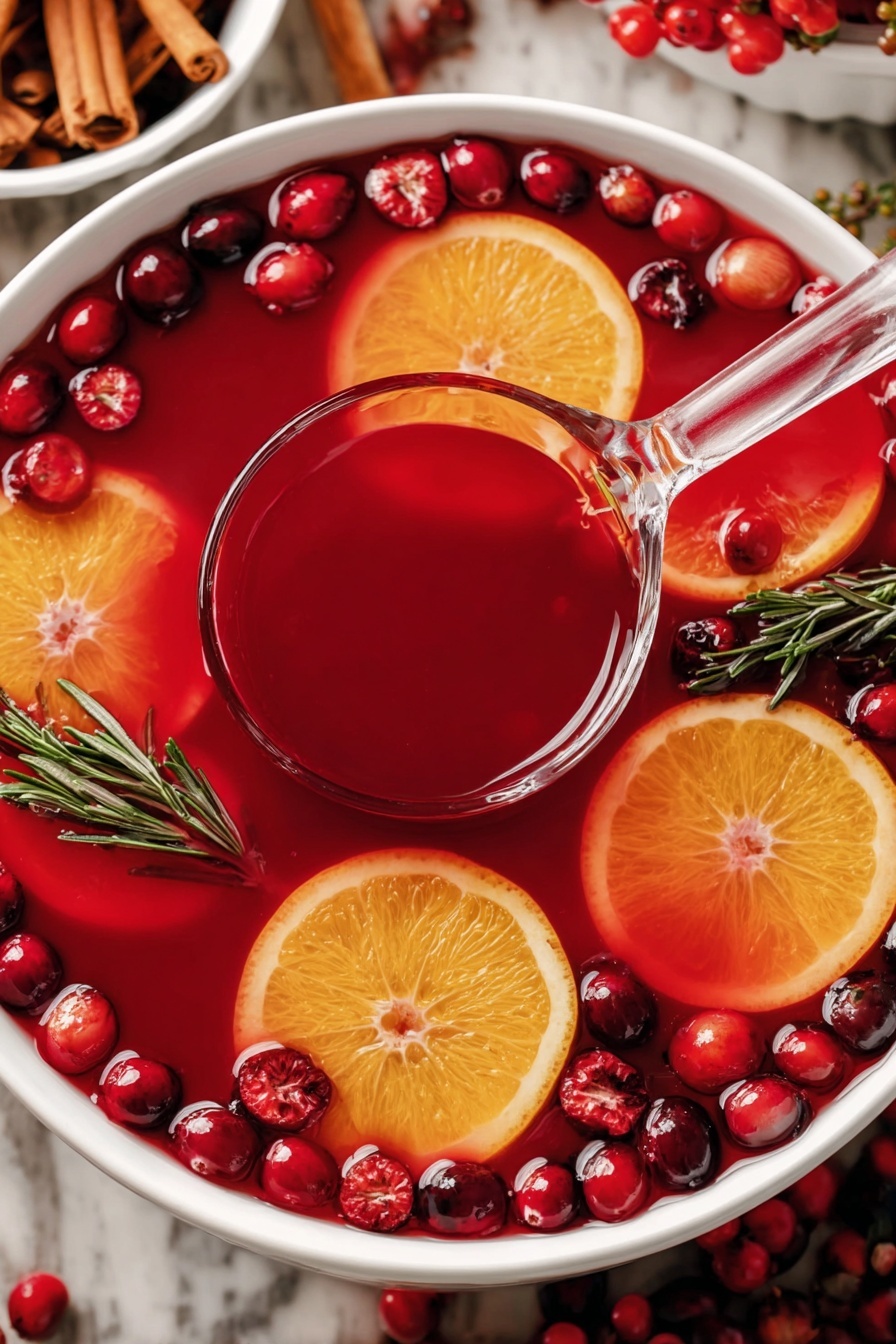 A large white bowl filled with deep red punch with floating layers of orange slices with bright yellow edges, red cranberries scattered throughout, and sprigs of green rosemary placed on the surface. A clear ladle filled with the red punch is resting inside the bowl, slightly above the orange slices and cranberries. The background is a white marbled surface with cinnamon sticks in a white bowl visible on the top left corner. photo taken with an iphone --ar 2:3 --v 7