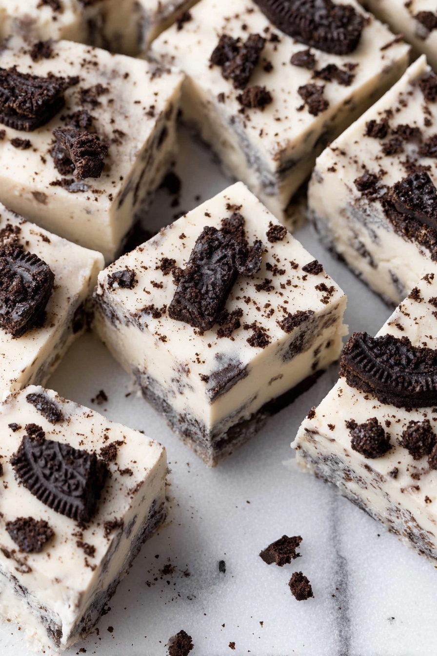 The image shows close-up squares of cookies and cream fudge, with one thick layer of creamy white fudge mixed evenly with small dark chocolate cookie pieces inside, topped with larger broken pieces of dark chocolate cookies scattered on the surface for texture. The fudge squares are arranged close together on a white marbled surface. The overall look contrasts the smooth, pale white base with dark cookie bits, giving a rich and textured appearance. photo taken with an iphone --ar 2:3 --v 7