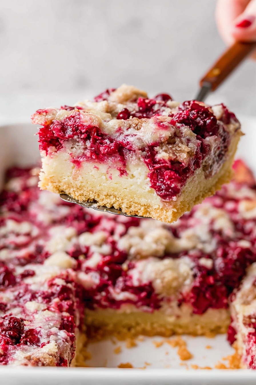 A square piece of dessert bar sits in the middle of a stack of four white plates. The dessert has three layers: the bottom layer is light beige and crumbly, the middle layer is filled with bright red whole cranberries, and the top layer has a light, slightly golden crust sprinkled with more cranberries and a dusting of powdered sugar. The background shows the full dessert in a white rectangular baking dish with handles, filled with the same three-layered dessert. Around the plates are scattered fresh cranberries, dark red grapes, and bright orange fruit slices on a white marbled surface. Photo taken with an iphone --ar 2:3 --v 7
