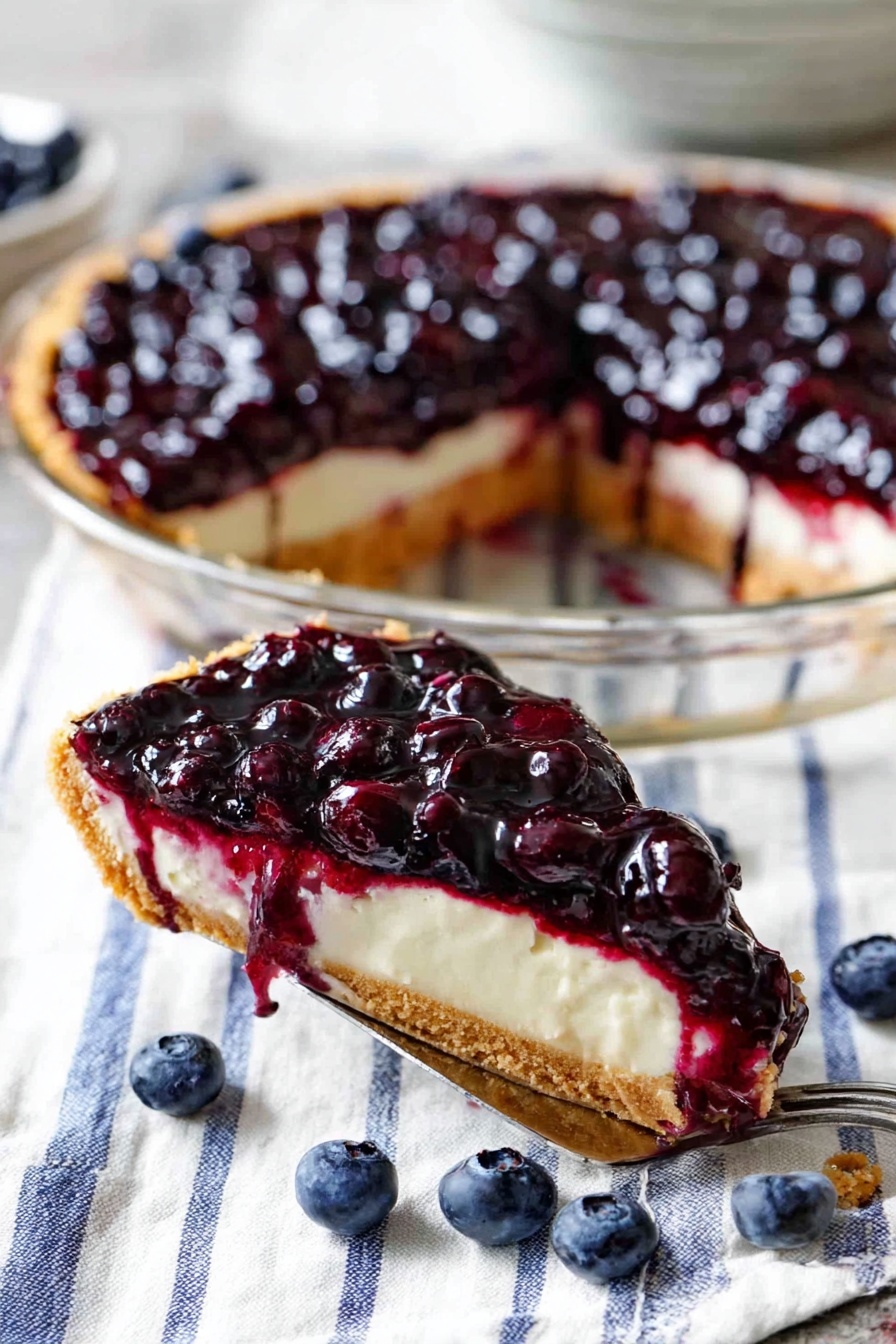 The image shows a blueberry cheesecake in a clear glass pie dish. It has three layers: the bottom layer is a golden crust, the middle layer is a creamy off-white cheesecake, and the top layer is a thick, shiny, deep purple blueberry topping with whole blueberries visible. A slice is missing, revealing the inside layers, and some blueberry sauce drips down the side of the cheesecake. In the background, there is a white plate with a slice of the cheesecake and a fork beside it on a white marbled surface. Some loose blueberries are scattered around the pie dish, and the dish rests on a white cloth with thin blue stripes. The mood is bright and fresh. photo taken with an iphone --ar 2:3 --v 7