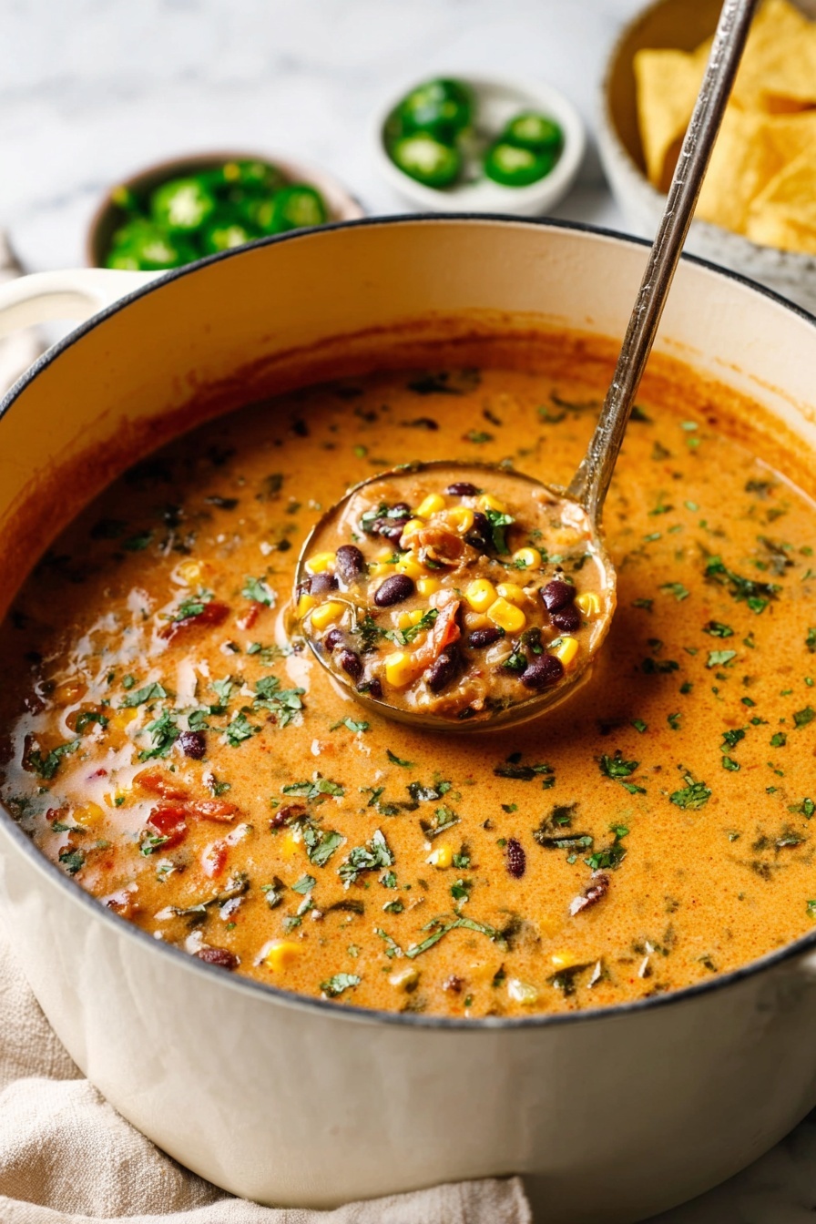 A close-up view of a white pot filled with a creamy orange soup mixed with visible pieces of black beans, bright yellow corn, and small green herbs sprinkled on top. The soup looks thick and textured with bits of red and green, likely from vegetables and spices. A ladle with a metallic handle is scooping a portion of the soup, showing the chunky ingredients and creamy consistency inside it. The pot rests on a soft beige cloth, with blurred bowls of green jalapeños and yellow tortilla chips in the white marbled background. Photo taken with an iphone --ar 2:3 --v 7