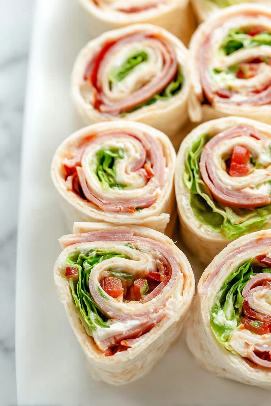 This image shows several small pinwheel sandwiches, each with multiple layers rolled tightly together. The outer layer is pale and smooth, likely a tortilla or flatbread, wrapping around layers of white creamy spread, light green crisp lettuce, thin slices of pinkish deli meat, and small bits of red pepper. The layers create a spiral pattern with varied colors of pale beige, creamy white, green, pink, and red. The rolls are placed close together side by side on a white plate over a white marbled surface. The photo taken with an iphone --ar 2:3 --v 7