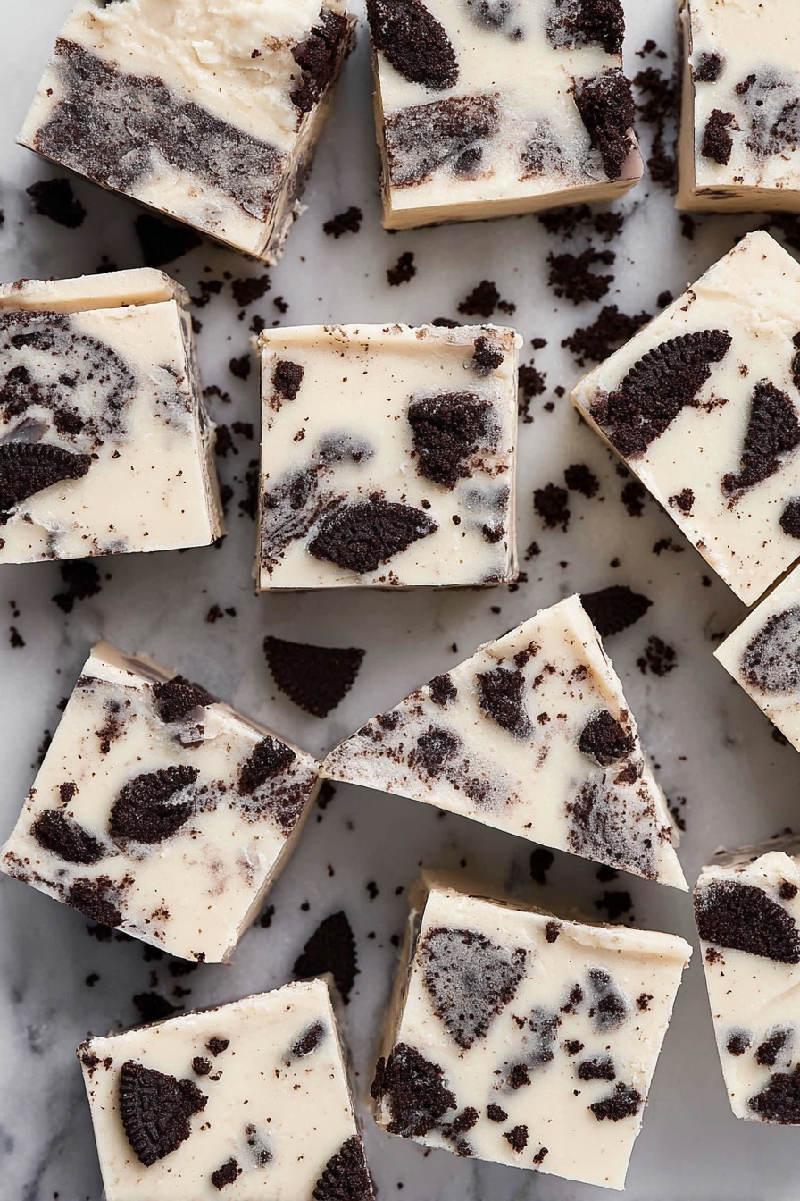 The image shows many square pieces of a white creamy fudge with dark chocolate cookie bits mixed in and scattered on top, each piece with a smooth, shiny top layer and chunks of dark cookie embedded throughout. The fudge squares are placed closely together on a white marbled surface, with some cookie crumbs scattered around, giving a nice contrast of dark brown pieces against the creamy white base. The pieces are uneven but mostly square with slightly rough edges, showing a creamy texture mixed with crunchy bits. photo taken with an iphone --ar 2:3 --v 7