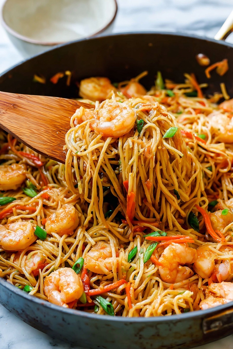 A close-up view of a pan filled with stir-fried noodles mixed with cooked shrimp and thin orange carrot strips, topped with small pieces of green onion. The noodles are light brown, soft-looking, and intertwined in layers throughout the pan. The shrimp are pink with a slight shine, scattered evenly among the noodles. A wooden spatula is lifting a portion of the noodles from the pan, showing texture and color contrast. The pan sits on a white marbled surface, with a small, partly visible white bowl in the background. photo taken with an iphone --ar 2:3 --v 7