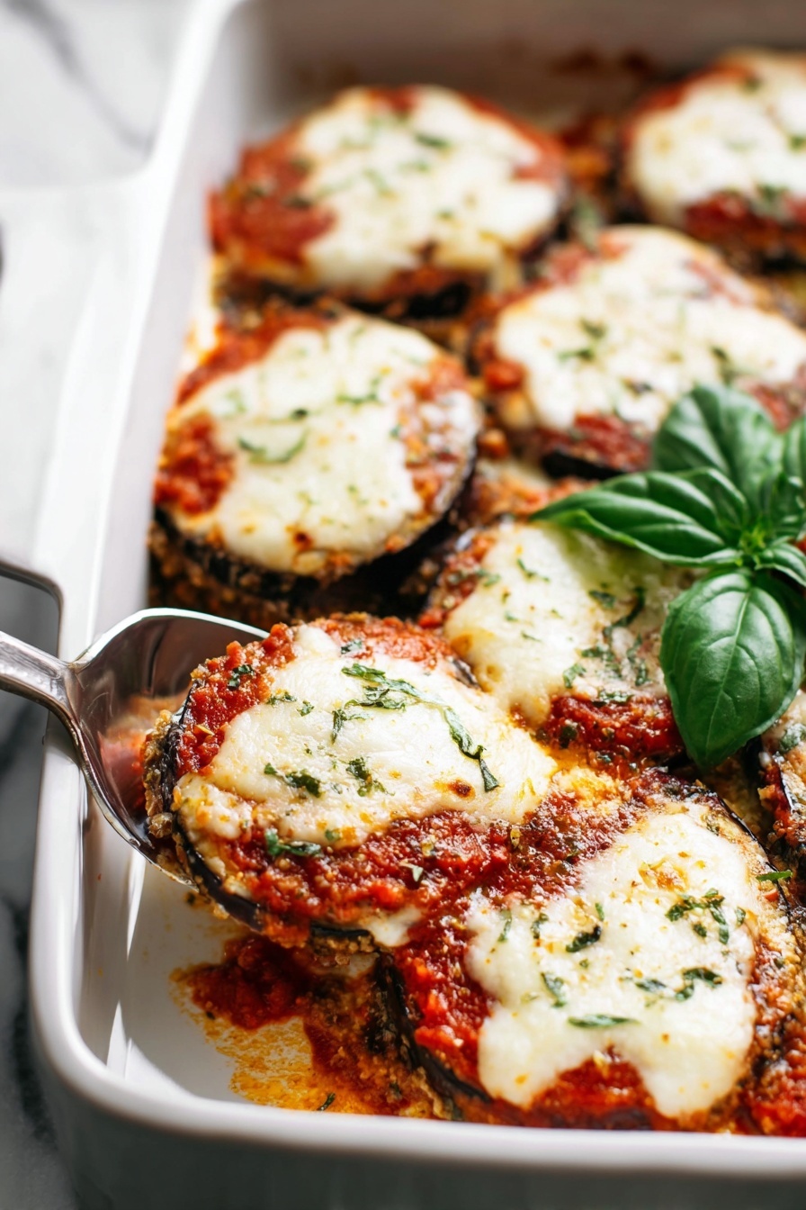 The dish shows several round slices of eggplant layered in a white baking dish. Each eggplant slice is topped with a layer of red tomato sauce, a thick melted white cheese layer that is slightly browned in spots, and some small green herb sprinkles across the top. The eggplant slices are stacked closely together, creating a rich, creamy, and saucy texture throughout. There is also a fresh green basil sprig placed on one side of the baking dish. A silver serving spoon is scooping one piece near the top left corner. The whole scene rests on a white marbled surface. photo taken with an iphone --ar 2:3 --v 7