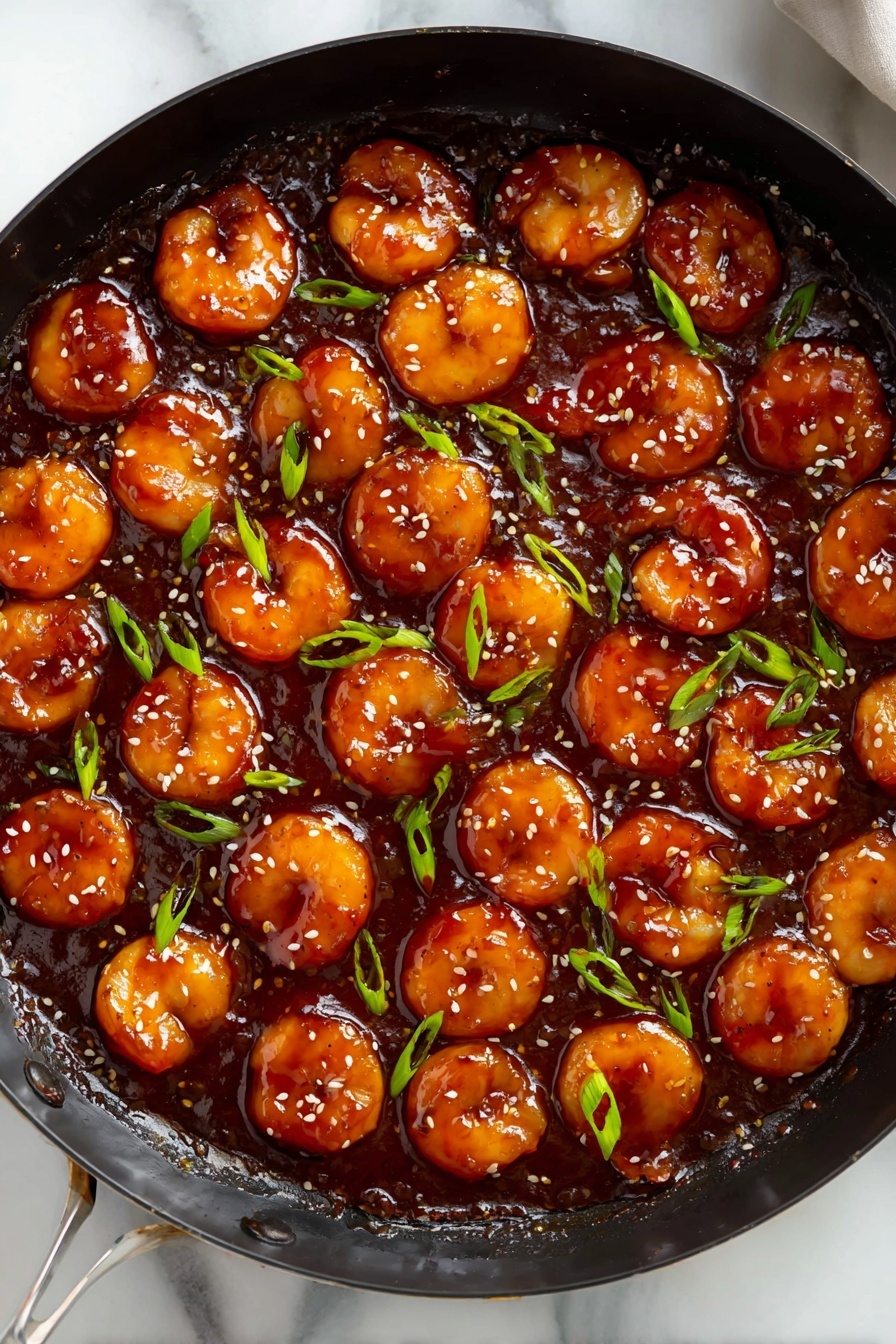 The image shows a black skillet filled with round, golden-brown pieces of food covered in thick, shiny dark red sauce. The pieces are evenly spread in a single layer, sitting in the rich sauce, which has a smooth and glossy texture. Green sliced scallions and small light brown sesame seeds are sprinkled over the top, adding spots of fresh green and light color against the dark sauce. The skillet is placed on a white marbled surface. photo taken with an iphone --ar 2:3 --v 7