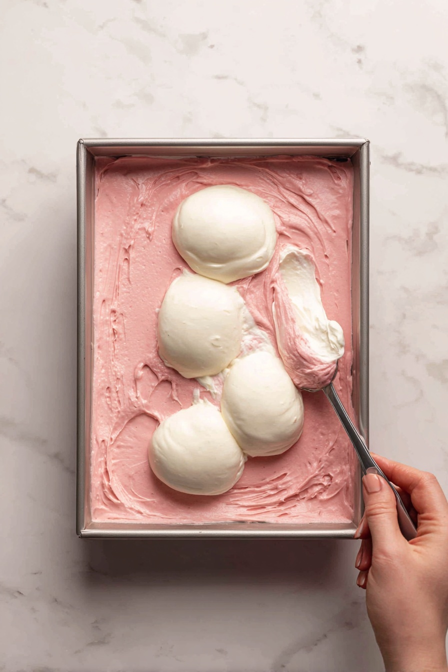 This image shows heart-shaped layered treats with three visible layers: the top and bottom layers are pink with a smooth texture, and the middle layer is creamy white. The treats are decorated on top with small, colorful heart-shaped sprinkles in red, white, and pink. One treat sits inside a white paper cupcake liner, and more treats are scattered on a white marbled surface in the background, some round and some heart-shaped. The scene is bright and softly focused. Photo taken with an iphone --ar 2:3 --v 7