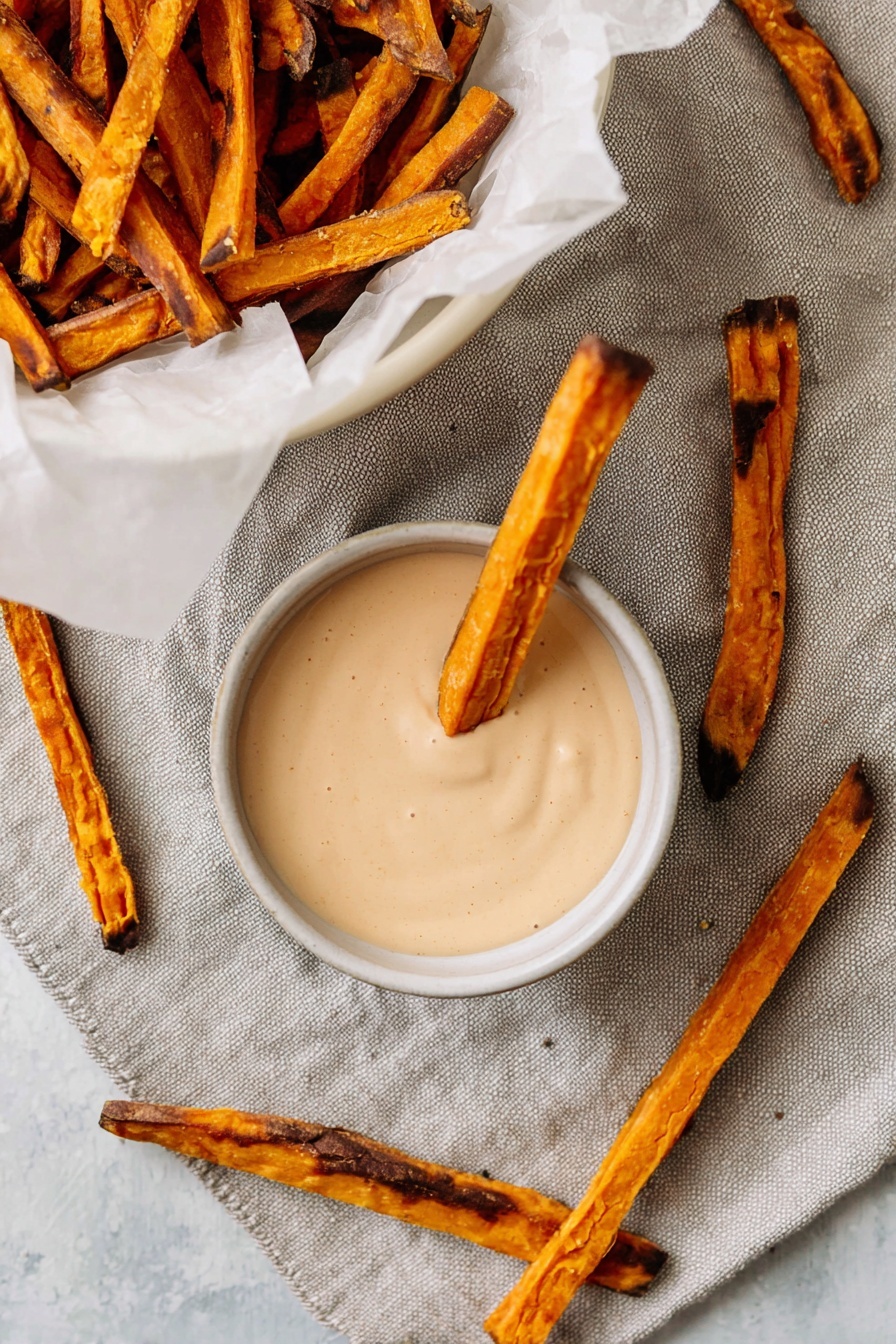 A dark bowl filled with many bright orange sticks of sweet potato, all cut in thick even lengths. The sweet potato sticks are sprinkled lightly with coarse white salt crystals. The bowl sits on a white marbled surface, giving a clean and simple look. The light shines softly on the orange sticks, showing their smooth texture. photo taken with an iphone --ar 2:3 --v 7