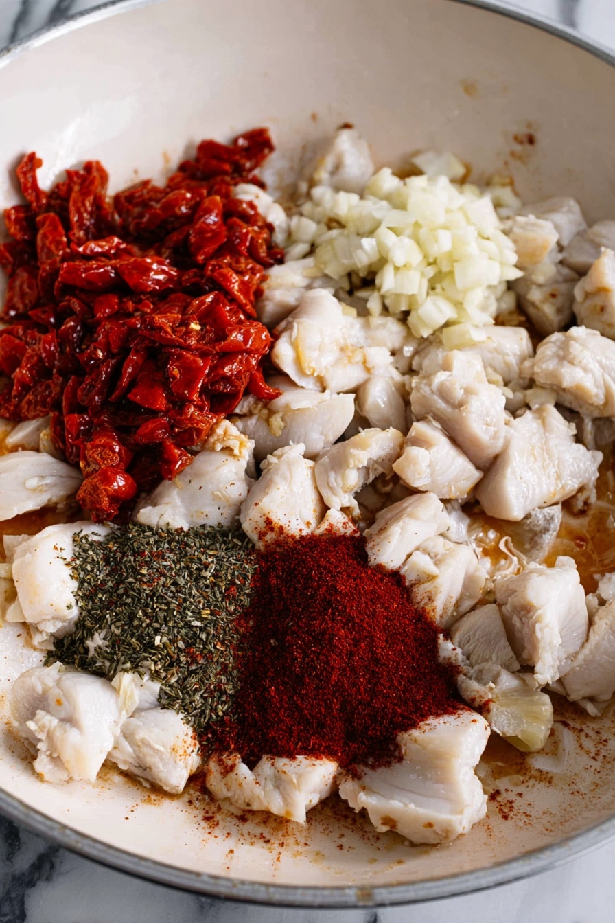 A round white bowl holds a creamy pasta dish with three main visible layers: the first layer is small rice-shaped pasta covered in light orange creamy sauce; the second layer includes pieces of white cooked chicken mixed throughout; the third layer features green spinach leaves and reddish sun-dried tomato strips scattered over the pasta. Black pepper is sprinkled on top, adding a speckled texture. A golden fork rests on the right side inside the bowl, with its prongs partially buried in the pasta. The bowl sits on a soft gray cloth on a white marbled surface. Photo taken with an iphone --ar 2:3 --v 7